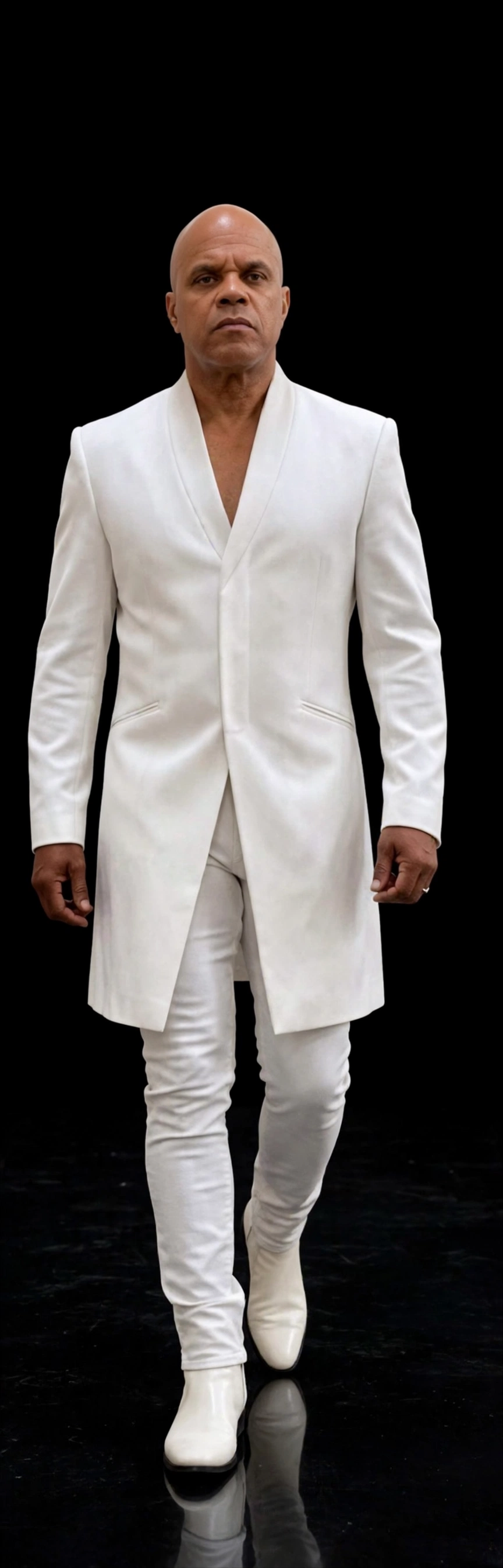 Tommy Holloway full-length in a white suit and white boots against a black backdrop, walking toward the camera